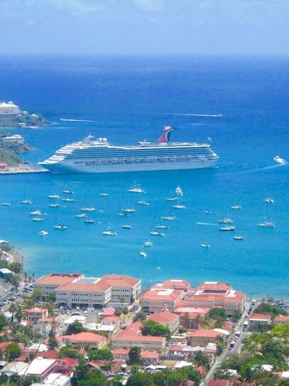 Scenic aerial view of a tropical harbor with cruise ships and sailboats in clear blue waters.